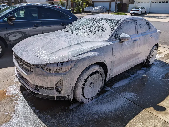 Vehicle covered in thick foam during a two-bucket hand wash on a driveway